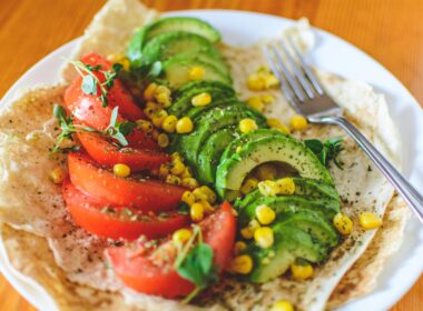 A vibrant salad with avocado, tomato, and corn on flatbread, topped with herbs, perfect for a healthy meal.