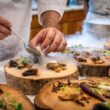 A chef artfully plating a gourmet dish with mushrooms and greens on wood slices.