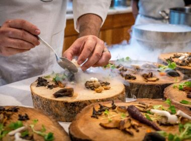 A chef artfully plating a gourmet dish with mushrooms and greens on wood slices.