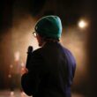 Moody scene of a performer holding a microphone under a spotlight on stage.