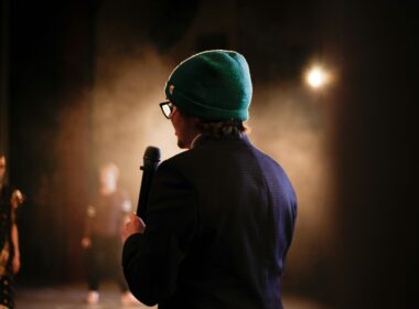 Moody scene of a performer holding a microphone under a spotlight on stage.