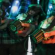 Close-up of players holding illuminated laser tag guns indoors.