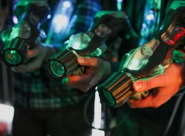Close-up of players holding illuminated laser tag guns indoors.